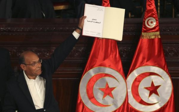 Tunisian President Marzouki holds a copy of the country's new constitution after signing it in Tunis