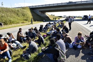 A group of refugees and migrants who were walking north sit down on the highway in southern Denmark on Wednesday, Sept. 9, 2015. The migrants have crossed the border from Germany, and after staying at a local school, they say they are now making their way to Sweden, to seek asylum. (Ernst van Norde/Polfoto via AP) DENMARK OUT